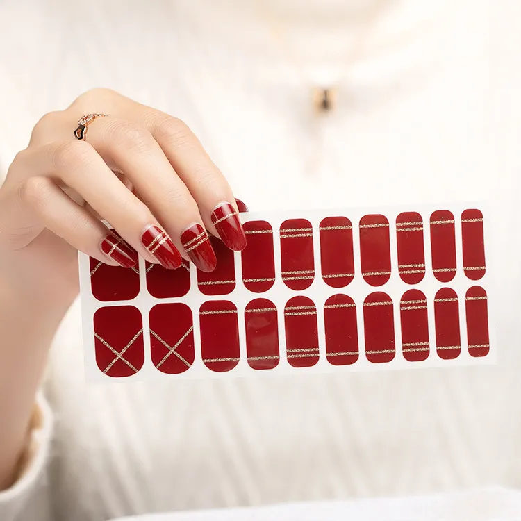 Hand with gold ring holding red-gold nail stickers on fabric