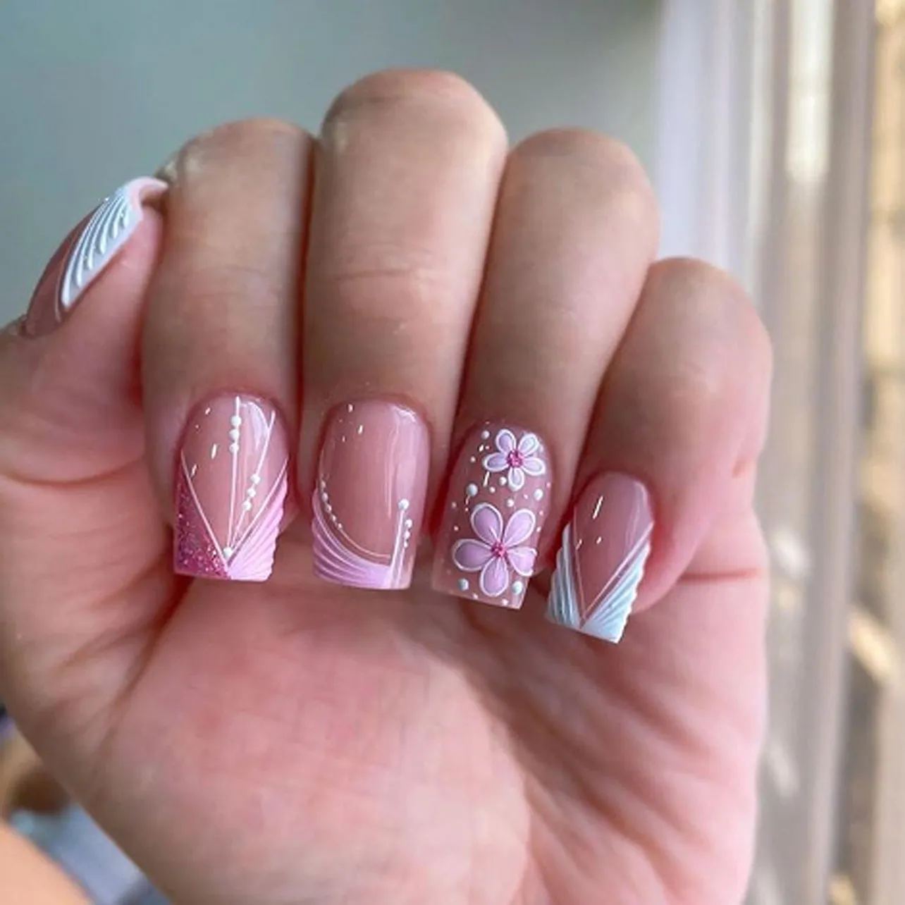 Nude nails with pink floral designs and glitter accents